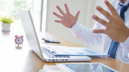 Man at computer with hands up looking like he made a marketing mistake